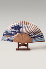 Abanico plegable japonés 'Ola de Kanagawa' sobre su soporte — gran ola azul con cresta de espuma blanca y varillas de bambú claro