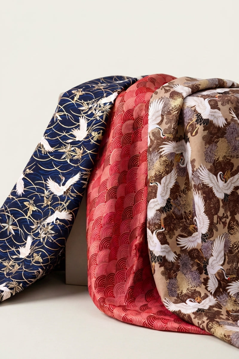 Colección furoshiki: tres pañuelos japoneses dispuestos uno junto a otro, grullas sobre azul noche, olas seigaiha rojas y crisantemos