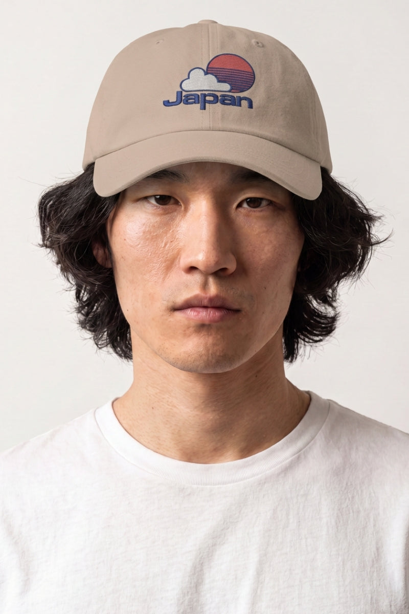 Colección de gorras japonesas: hombre con gorra beige bordada con un sol naciente, una nube y letras en azul y rojo