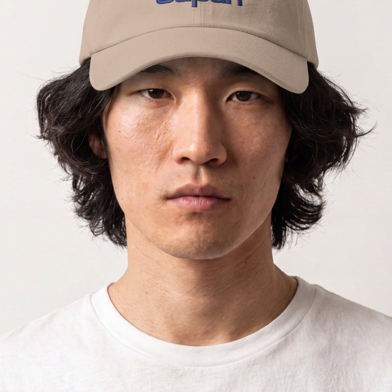 Colección de gorras japonesas: hombre con gorra beige bordada con un sol naciente, una nube y letras en azul y rojo