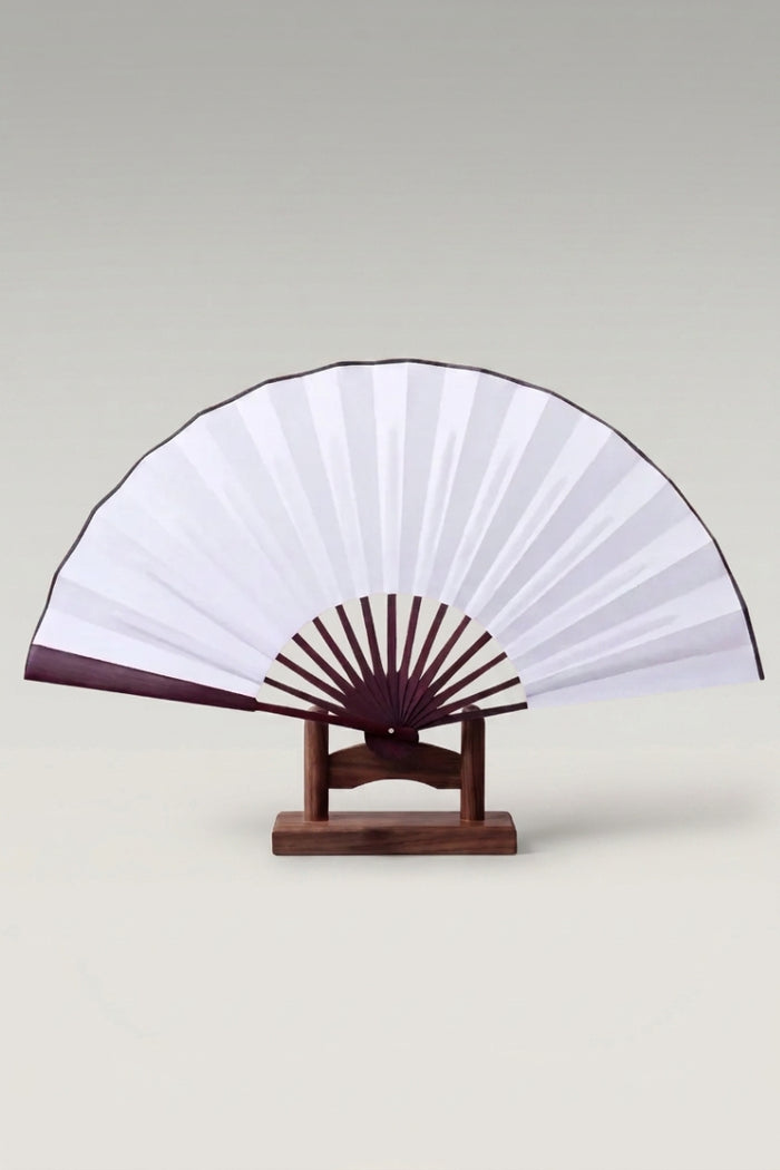 Abanico plegable japonés grande 'Kisho' sobre su soporte — hoja blanca con ribete oscuro y montura ancha visible de varillas espaciadas