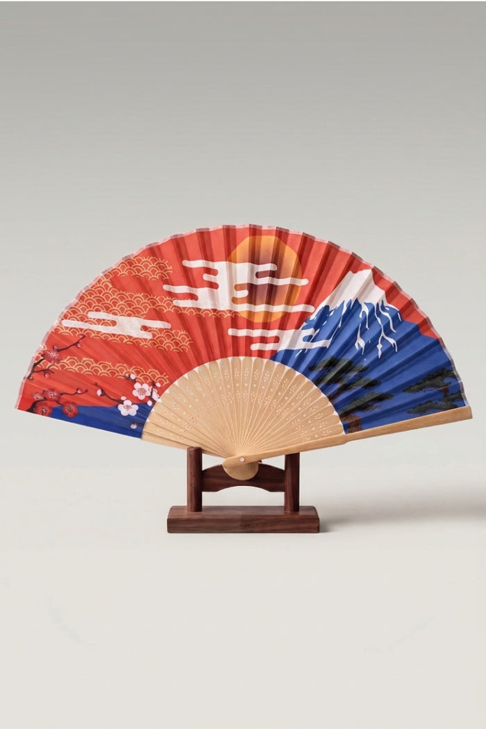 Abanico plegable japonés 'Minamato' abierto sobre su soporte — sol naranja, olas doradas y Monte Fuji azul sobre hoja rojo vivo