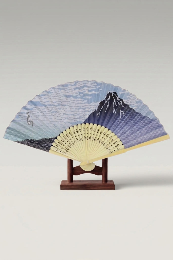 Abanico plegable japonés 'Ikoma' abierto sobre su soporte — Monte Fuji en acuarela bajo un cielo pálido y varillas de bambú pajizo caladas