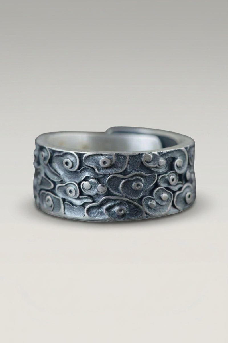Anillo 'Kochino' — anillo ancho con motivo de olas enroscadas y huecos realzados por una pátina azulada, foto de producto sobre fondo gris claro