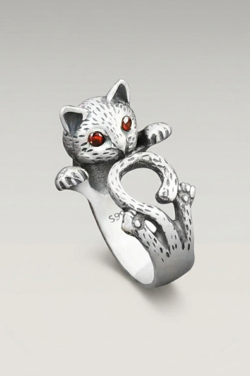 Anillo 'Shotika' — gato tallado en bulto redondo, con la pata alzada y ojos engastados en rojo, foto de producto sobre fondo gris claro