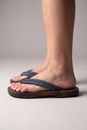 Chanclas japonesas vistas de perfil, calzadas descalzas — suela de madera plana y curvada, tira azul grisáceo con motivo de olas