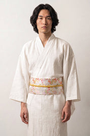 Cinturón obi 'Ume' ceñido a la cintura sobre un kimono blanco por un modelo masculino — fondo blanco con siembra de flores multicolores y cordón dorado a juego