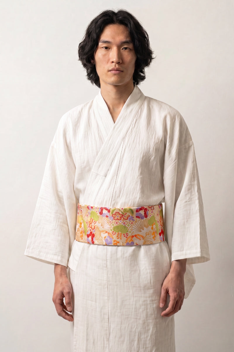 Cinturón obi 'Nanten' sobre un kimono blanco por un modelo masculino — fondo amarillo oro cubierto de flores multicolores y motivos de abanico