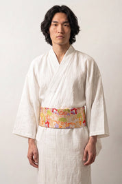 Cinturón obi 'Nanten' sobre un kimono blanco por un modelo masculino — fondo amarillo oro cubierto de flores multicolores y motivos de abanico