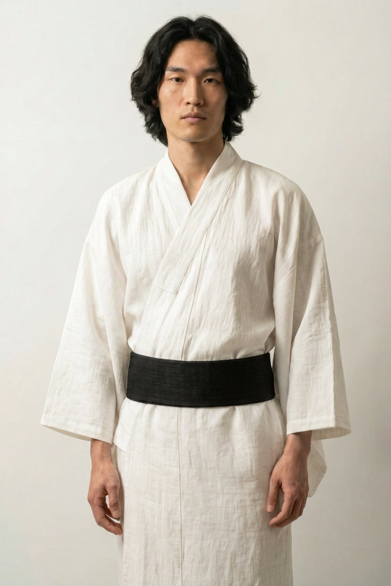 Cinturón obi 'Okinawa' ceñido a la cintura sobre un kimono blanco por un modelo masculino — tejido negro liso de superficie mate y ligeramente granulada