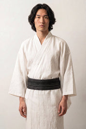 Cinturón obi 'Nahako' ceñido a la cintura sobre un kimono blanco por un modelo masculino — negro atravesado por rayas blancas finas y espaciadas