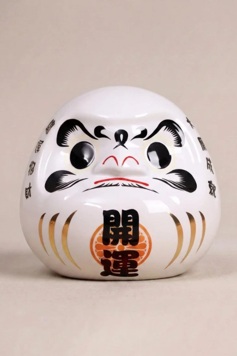 Daruma blanco de cerámica sobre fondo beige — figura redonda de 11 cm con el kanji 神, ojos en blanco para el rito del deseo