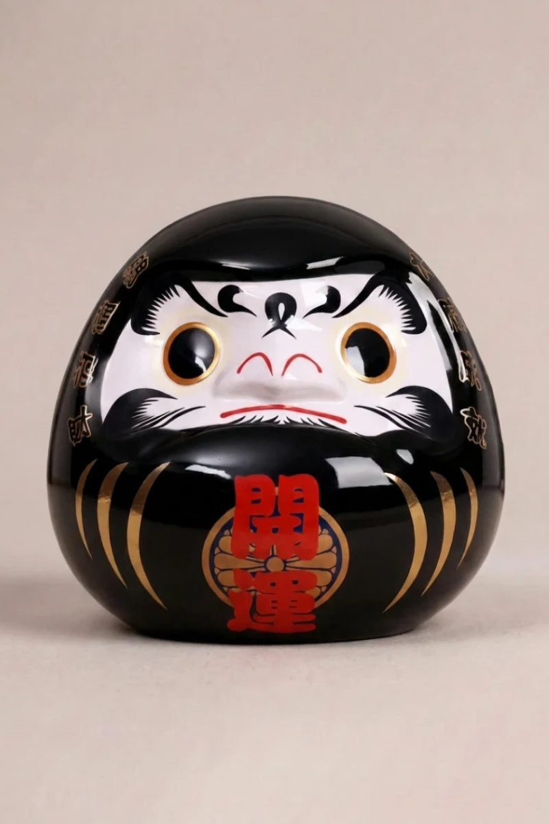 Daruma negro sombra de cerámica sobre fondo beige — figura redonda de 11 cm con el kanji 影, ojos en blanco para el rito del deseo