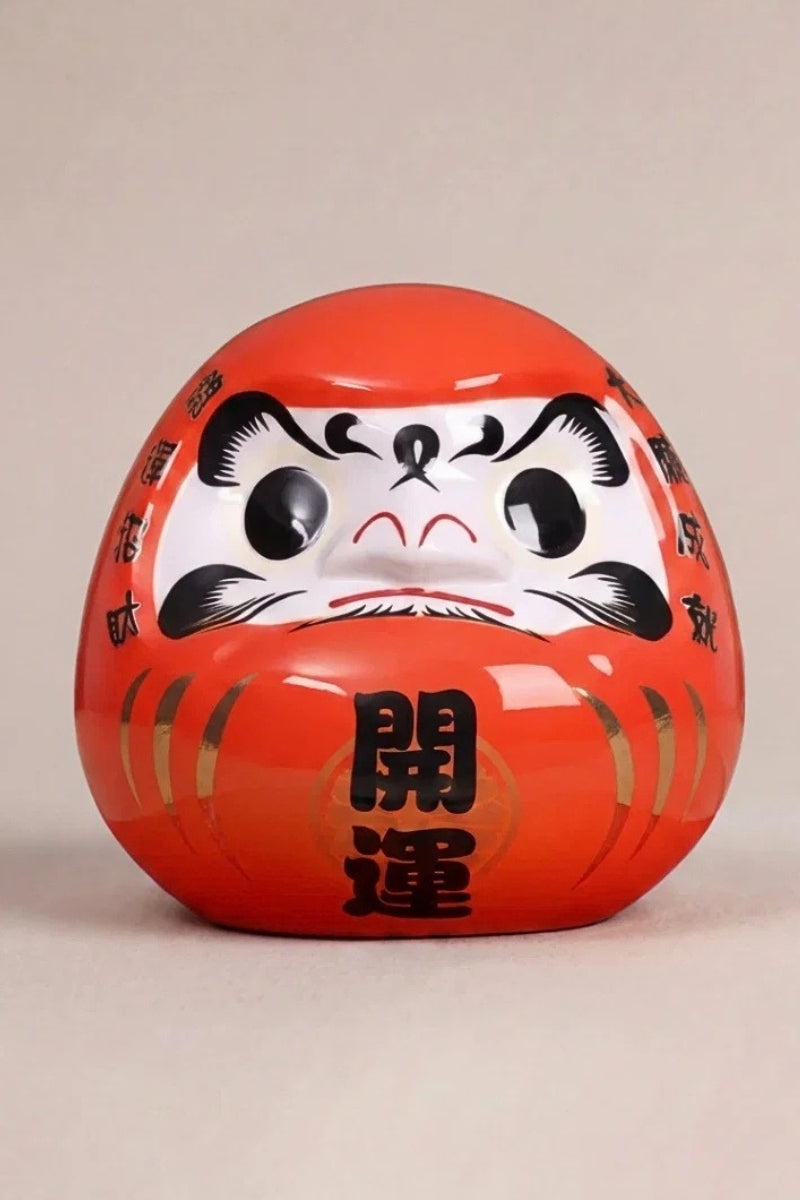 Daruma rojo de cerámica sobre fondo beige — figura redonda de 11 cm con el kanji 将, ojos en blanco para el rito del deseo