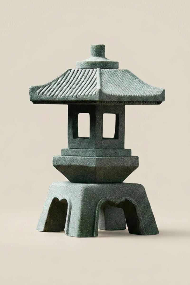 Farol japonés — farol de piedra verde grisáceo con tejado estriado en pendiente, cuerpo hexagonal calado y patas en arco, foto sobre fondo beige