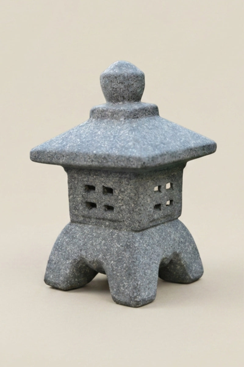 Farol japonés — farol de jardín gris con tejado cuadrado sobrio, cuerpo perforado con ventanitas y cuatro patas curvas, foto de producto sobre fondo beige liso