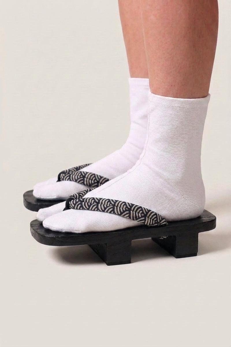 Geta japonés 'Shinshiro' calzada con calcetines tabi blancos, vista de perfil — plataforma de madera teñida de negro, tira con motivo de olas en blanco y negro