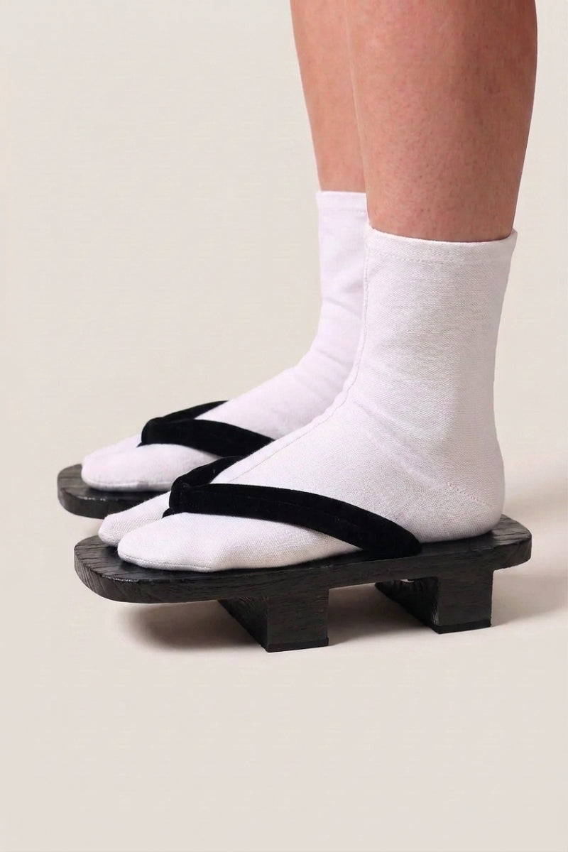 Geta japonés 'Hekinan' calzada con calcetines tabi blancos, vista de perfil — plataforma de madera teñida de negro, tira negra mate a juego con la base