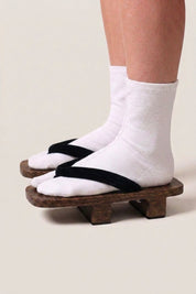 Geta japonés 'Iwakura' calzada con calcetines tabi blancos, vista de perfil — plataforma de madera oscura, tira negra lisa