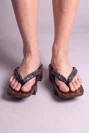 Geta japonés 'Okazaki' calzada con los pies descalzos, vista frontal — tira caqui con motivo discreto sobre plataforma alzada de madera oscura