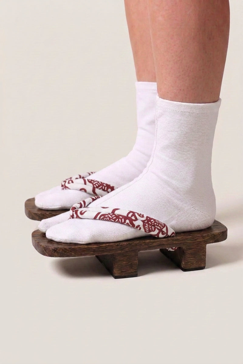 Geta japonés 'Shakori' calzada con calcetines tabi blancos, vista de perfil — plataforma de madera oscura, tira rojo profundo con motivo de cachemira blanco