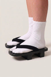 Geta japonés 'Tsushima' calzada con calcetines tabi blancos, vista de perfil — plataforma de madera teñida de negro, tira negra fina y flexible