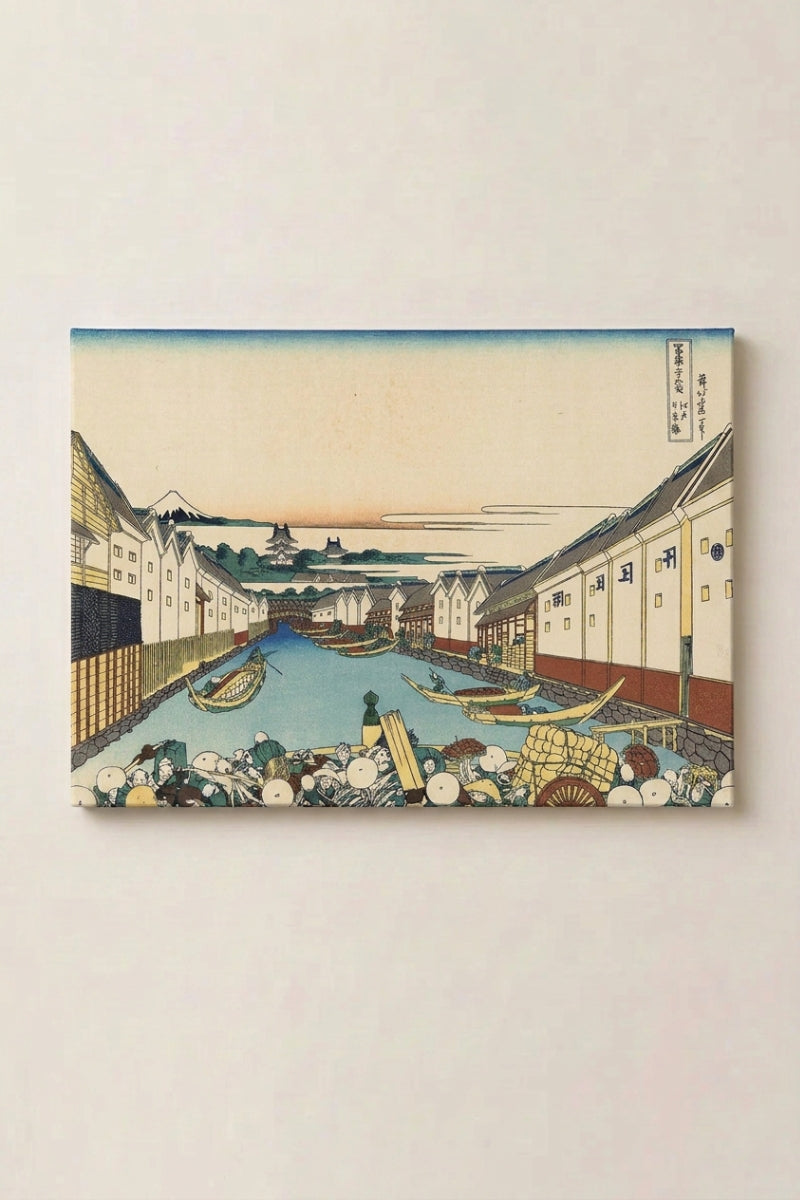 Grabado japonés 'Onikawa' en panel enmarcado sobre pared beige — calle de comerciantes con almacenes blancos junto a un canal lleno de barcas y el Fuji al fondo