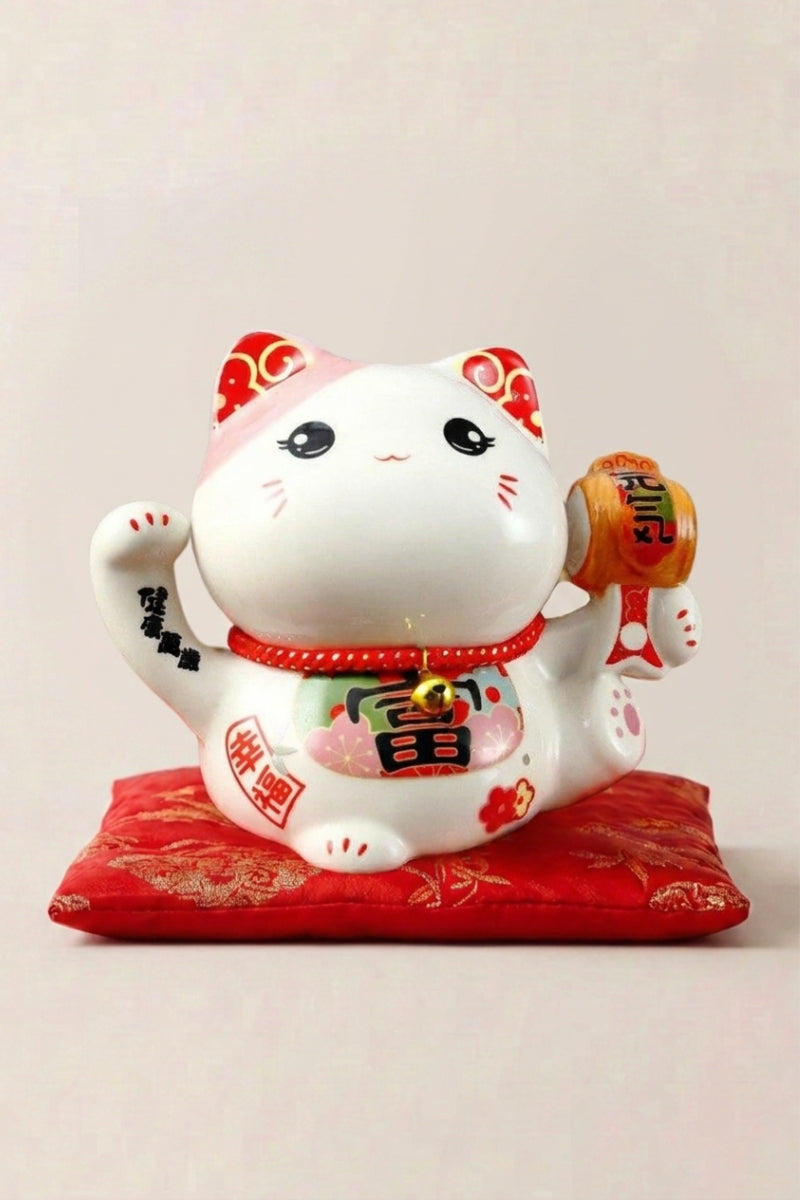 Hucha maneki neko 'Success' de cerámica — gato blanco con collar rojo sosteniendo una placa dorada y ambas patas alzadas, sobre un cojín rojo