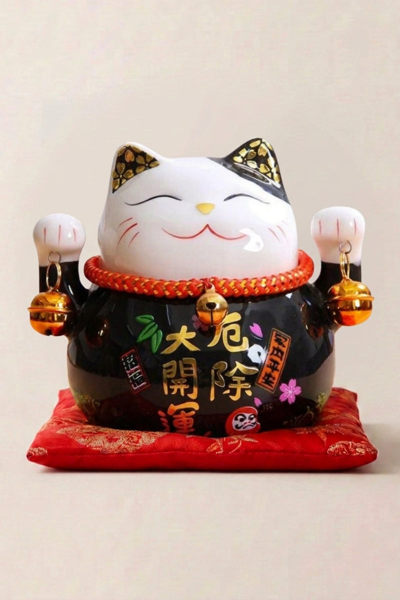 Hucha maneki neko 'Black' de cerámica — gato negro lacado con decoración dorada y placa caligrafiada, ambas patas alzadas, sobre un cojín rojo