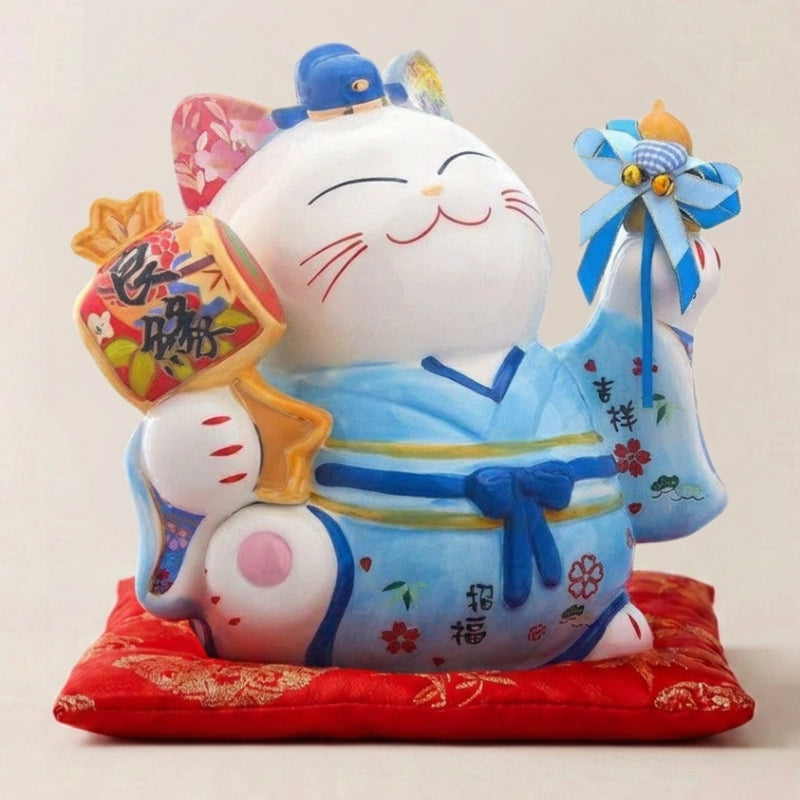 Hucha maneki neko 'Blue Fortune' de cerámica — gato azul con kimono y lazo, saco de la fortuna al hombro y pata derecha alzada, sobre un cojín rojo