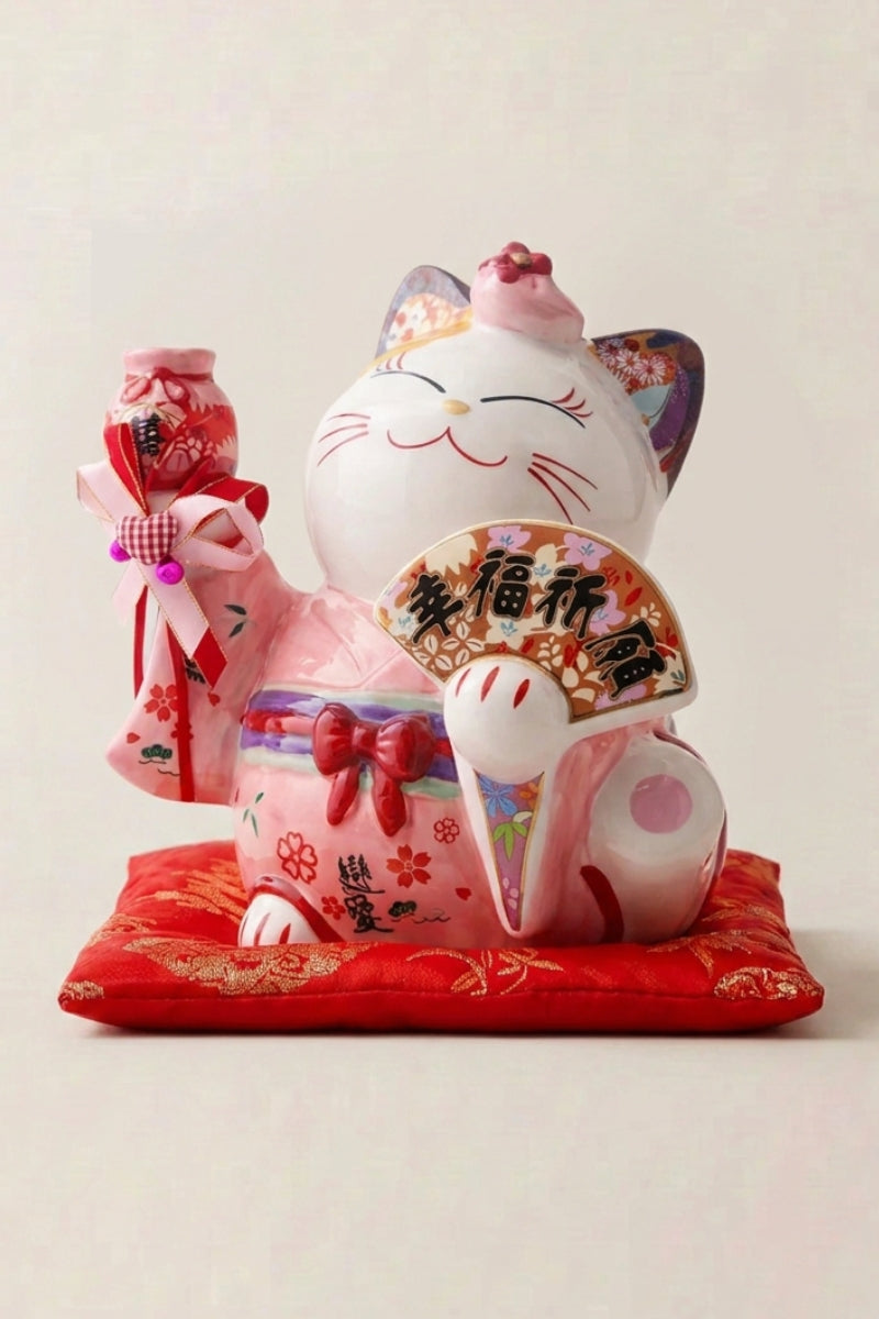 Hucha maneki neko 'Pink Fortune' de cerámica — gato rosa sembrado de flores y abanicos, pata derecha alzada, formato grande, sobre un cojín rojo