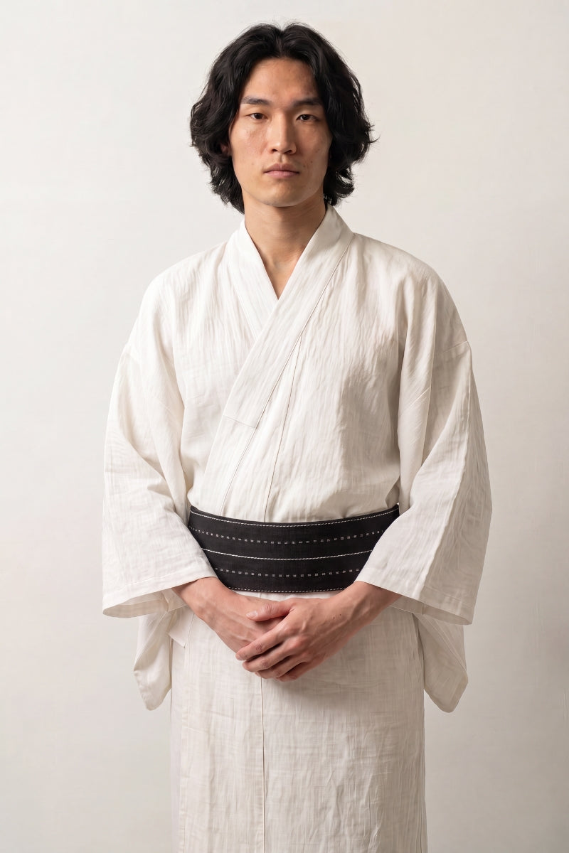 Cinturón obi 'Nagano' ceñido a la cintura sobre un kimono blanco por un modelo masculino — fondo azul noche recorrido por finas rayas blancas de puntos