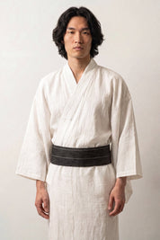 Cinturón obi 'Hikoma' ceñido a la cintura sobre un kimono blanco por un modelo masculino — verde oscuro casi negro con finas rayas verticales en el tejido