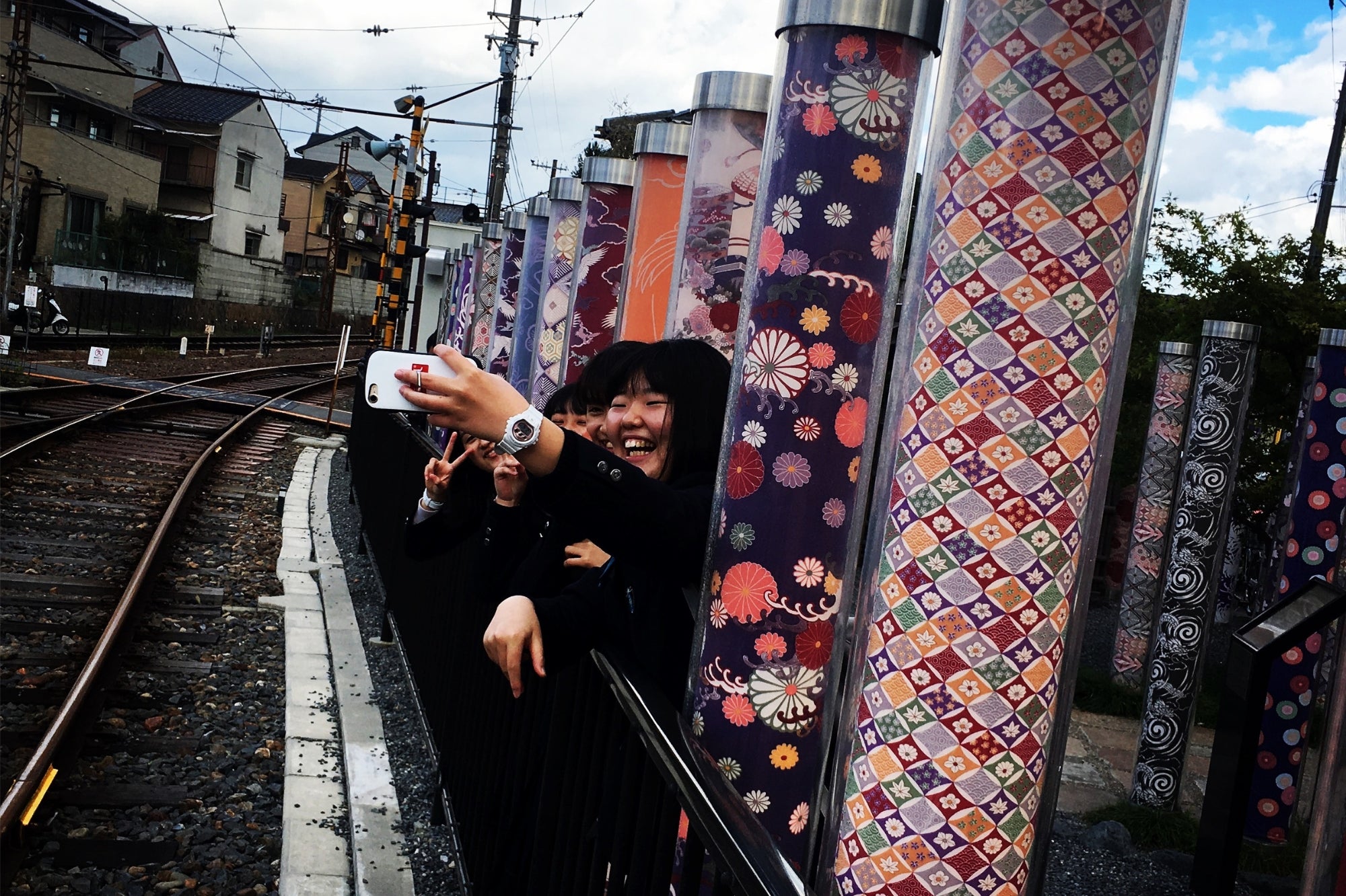 Grupo de estudiantes japonesas sonrientes tomándose un selfie entre las columnas luminosas de Arashiyama en Kioto, símbolo del Japón moderno y colorido.