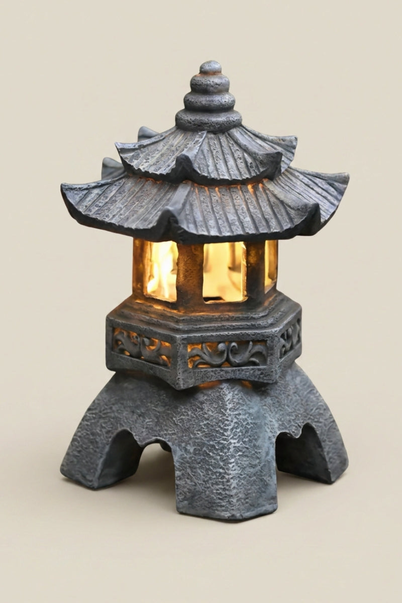 Farol japonés — farol de jardín gris con tejado escalonado y friso tallado, ventanas iluminadas con luz ámbar, foto de producto sobre fondo beige liso