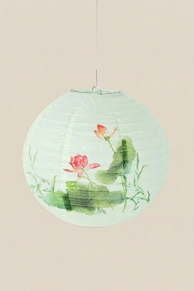 Farol japonés color flor de loto — farol esférico de papel verde agua con un loto rosa y hojas anchas, colgado de un hilo sobre fondo beige liso