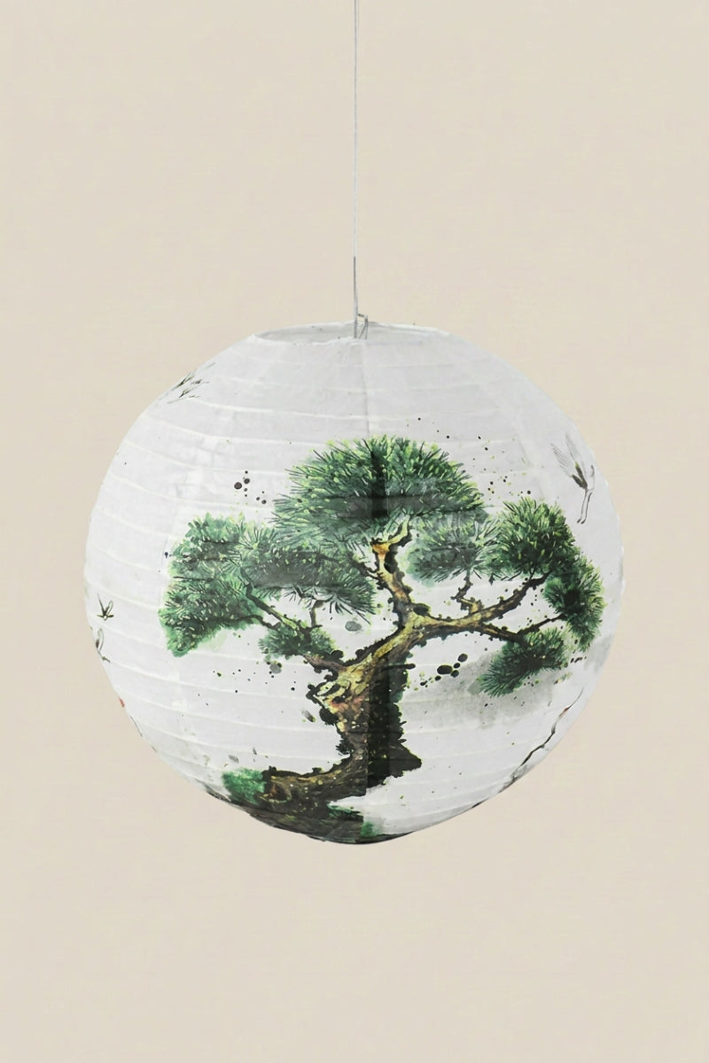Farol japonés color árbol — farol esférico de papel blanco con un pino nudoso pintado en tinta verde y negra, colgado de un hilo sobre fondo beige liso