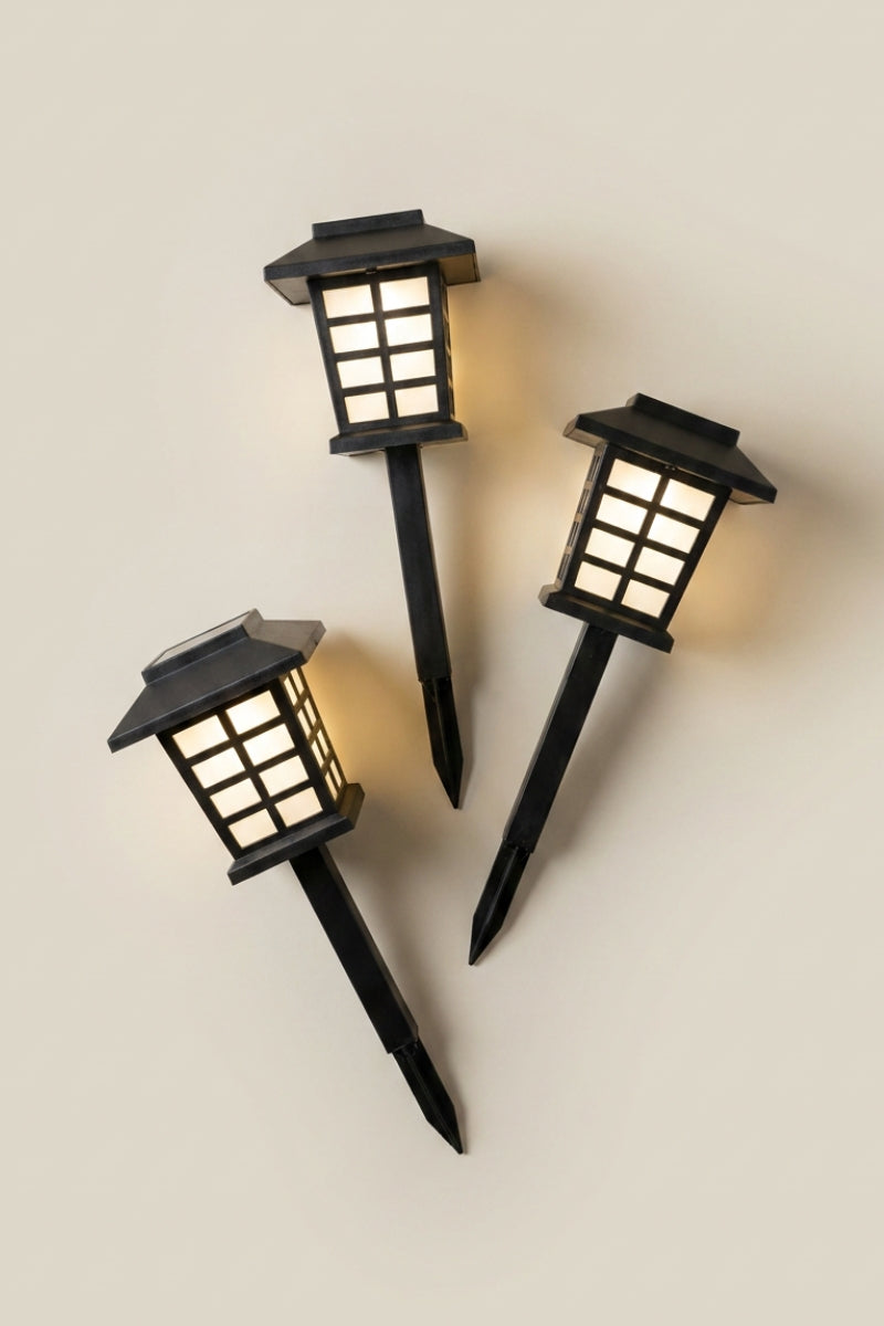 Farol japonés — tres faroles LED negros con pincho, cristales blancos encendidos y tejado piramidal sobre fondo claro, foto de producto sobre fondo beige liso