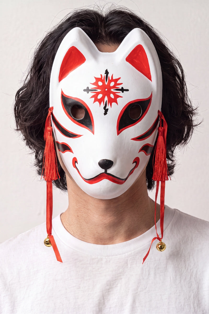 Máscara kitsune con estrella llevada por un modelo sobre fondo claro — zorro blanco con una estrella roja en la frente, trazos finos y cordones rojos