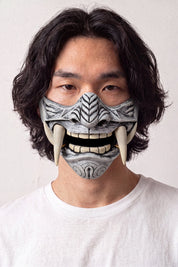 Media máscara mempō plateada llevada por un modelo sobre fondo claro — protección gris plata grabada con motivos en relieve, dientes visibles y colmillos