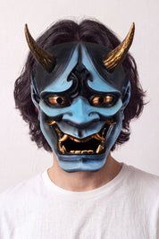 Máscara hannya azul llevada por un modelo sobre fondo claro — demonio azul con cuernos dorados, cejas fruncidas y boca abierta con colmillos
