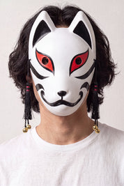 Máscara kitsune blanca y negra llevada por un modelo sobre fondo claro — zorro blanco con orejas y contornos negros, hocico rojo y borlas negras