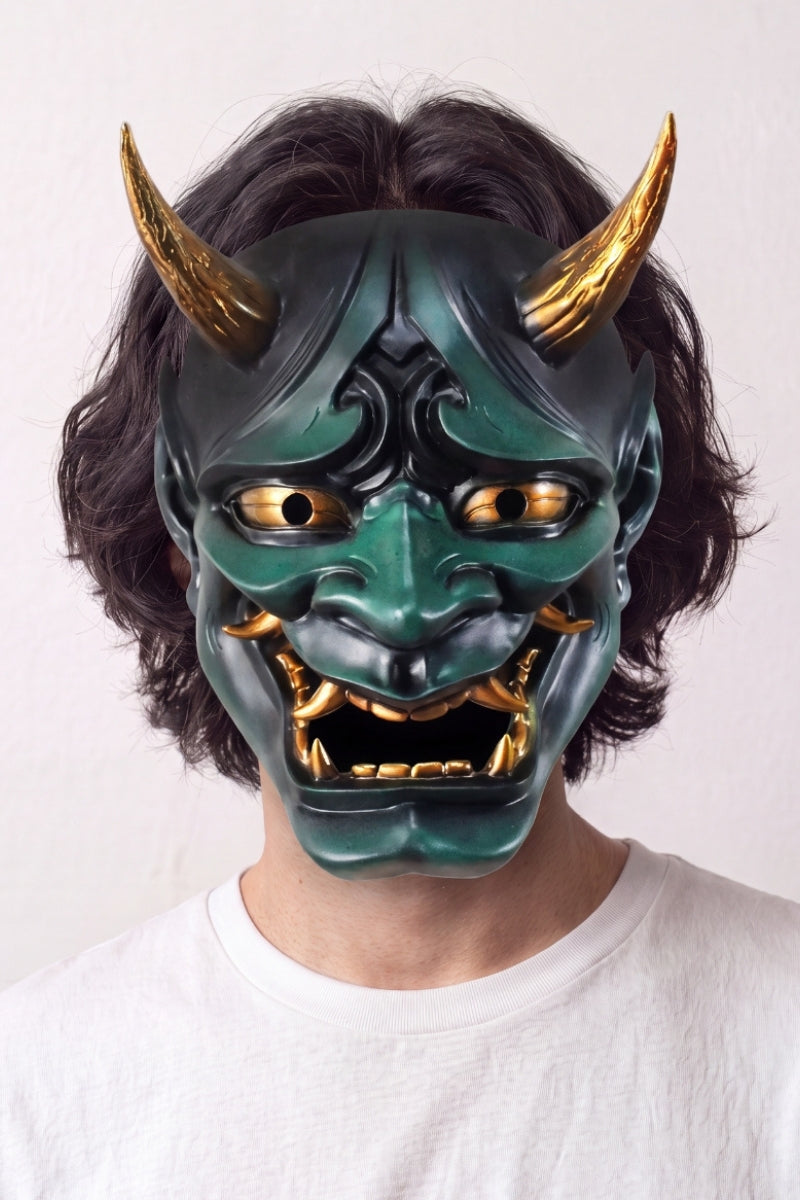 Máscara hannya verde llevada por un modelo sobre fondo claro — demonio verde con cuernos dorados, ojos saltones y mandíbula abierta con colmillos