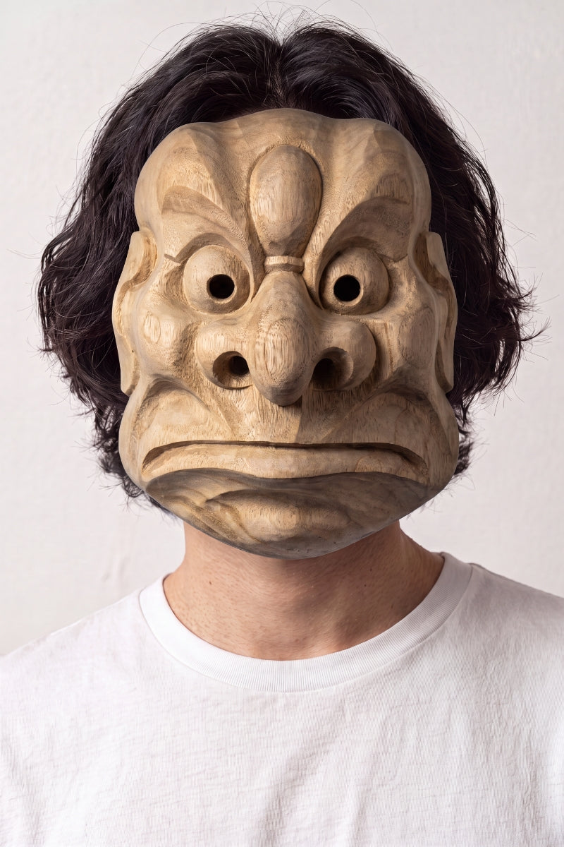 Máscara tengu karasu llevada por un modelo sobre fondo claro — tengu cuervo tallado con pico prominente, ojos grandes y frente nervada