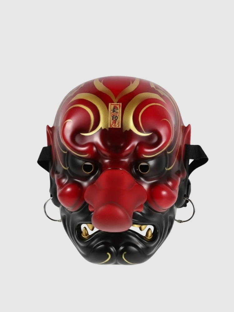 Máscara tengu rojo presentada de frente sobre fondo gris liso — nariz larga y prominente, cejas en volutas doradas y colmillos blancos
