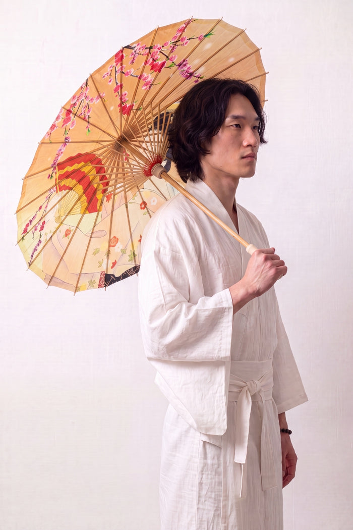Sombrilla japonesa 'Kuki-Fan' abierta y sostenida por un modelo con kimono blanco — tela naranja sembrada de abanicos abiertos y una grulla en vuelo