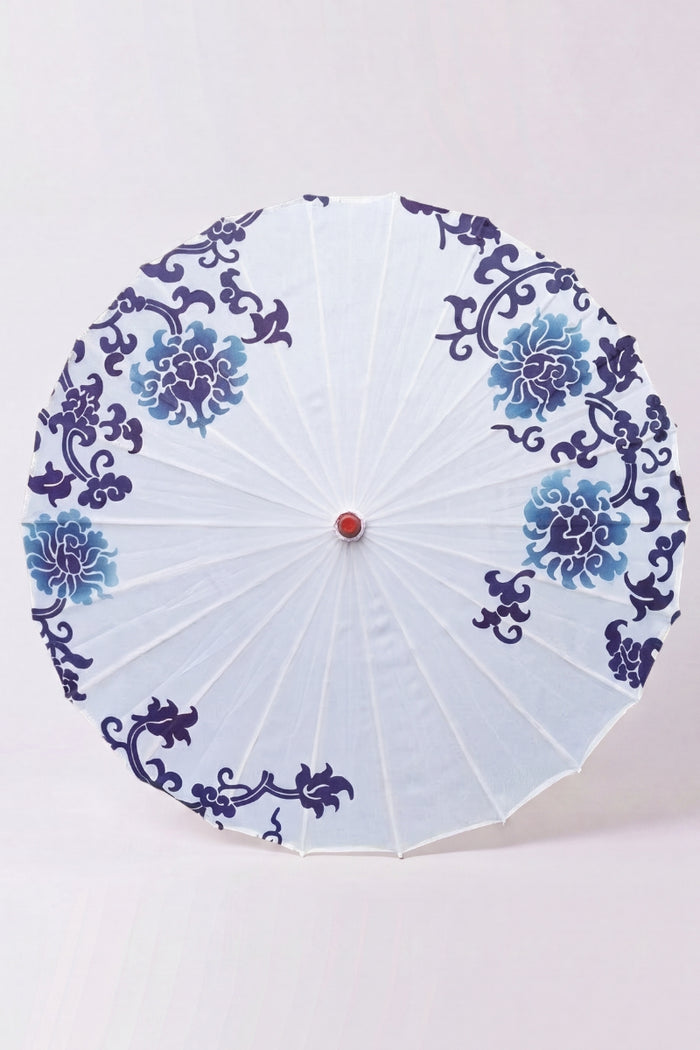 Sombrilla japonesa 'Shiroi' vista desde arriba, abierta en plano — tela blanca con motivo floral azul dispuesto en corona, varillas que irradian desde el buje