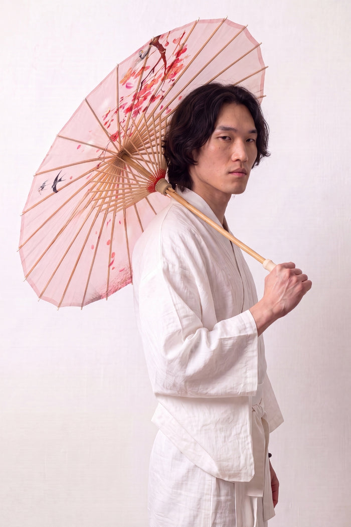 Sombrilla japonesa 'Sakura Classic' abierta y sostenida por un modelo con kimono blanco — tela rosa pálido con pájaros y ramas finas en flor