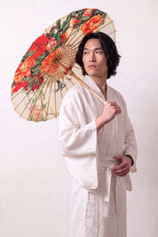 Sombrilla japonesa 'Asatsuyu' abierta y sostenida por un modelo con kimono blanco — tela crema con grandes flores naranjas y rojas