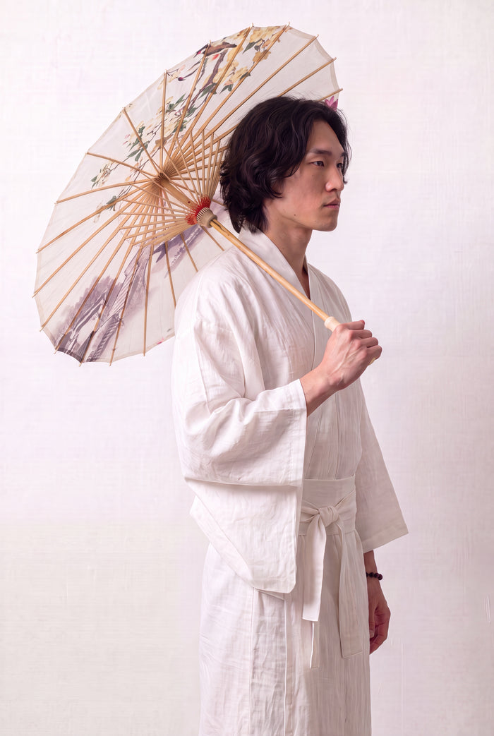 Sombrilla japonesa 'No-Kodai' abierta y sostenida por un modelo con kimono blanco — tela crema con rama florida rosa sobre fondo libre